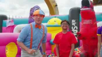 Blippi's Ultimate Bounce House Challenges TV: Blippi stands next to a boy wearing a red shirt and a red inflatable dinosaur.