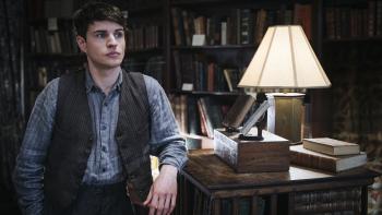 Bookish TV show screenshot 2: Connor Finch leans against a shelf in a bookstore. He wears a blue striped shirt, black striped vest, and dark pants.