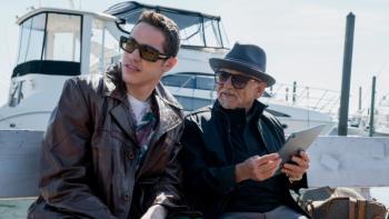 Bupkis TV show screenshot: Joe and Pete sit together in front of a large yacht; both wear sunglasses and black clothing and are looking at something off-camera