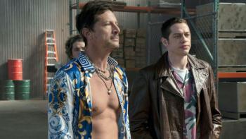 Bupkis TV show screenshot: Pete and a friend stand in a living room together; Pete wears a leather jacket, his friend wears a shirt open to the waist