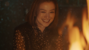 Burn the House Down TV show  screenshot 2: Makiko sits in front of a fire smiling broadly. 