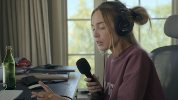 Call Her Alex TV show screenshot 1: Alex Cooper recording her podcast in pink sweater.