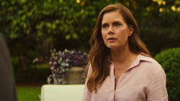 Cape Fear TV show screenshot 1: Amy Adams stands outside in flush greenery. She wears a light pink shirt and a necklace.