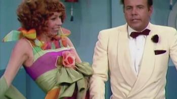 The Carol Burnett Show screenshot 2: Two actors from the Carol Burnett show appear in a skit. A redheaded woman appears at left in a pale green and purple dress with ruffles, while a man in a white suit stands on the right with a perplexed expression.