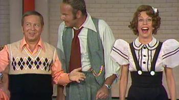 The Carol Burnett Show screenshot 4: Three actors from the Carol Burnett show appear in a skit. Two men stand on the left, engaged in conversation, while Carol Burnett stands at right with a big grin on her face.