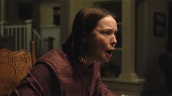Carrie's mother Margaret is shown sitting in a dimly lit room, appearing upset and animated.