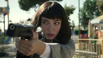 Matilda De Angelis aims a gun while looking off to the side. She wears a beige coat and a white button-up shirt.