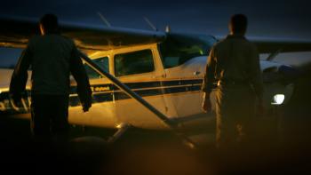 Cocaine Bear: The True Story: two men walk toward a small private plane at dusk.