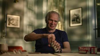 Cold Case: The Tylenol Murders screenshot 2: James Lewis tries to peel the foil seal off an uncapped Tylenol bottle. He wears a dark blue T-shirt.