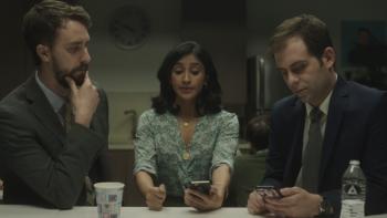 Corporate TV Show: Two men and a woman sit in an office breakroom; one o the men and the woman are looking at their phones. 