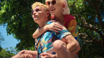 Couple to Throuple TV show screenshot 1: A man in colorful shirt carries female partner on his back. 