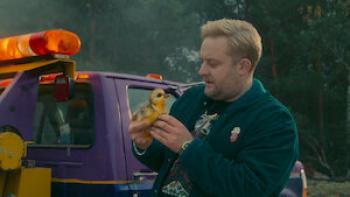 Crap Happens TV show screenshot 2: Man holding a small duck toy beside a purple tow truck.