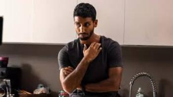 Akshay Kanna leans against the countertop in a kitchen. He wears a dark grey T-shirt and a black watch.