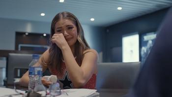 America's Sweethearts TV show screenshot 2: A brunette cheerleader in a red top sits at a table in an office, wiping tears.