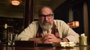 Death and Other Details Screenshot #2: Mandy Patinkin sits at a table with a serious look on his face