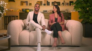 The two stars of Designing Miami sit on a puffy couch, smiling at the camera while conversing.