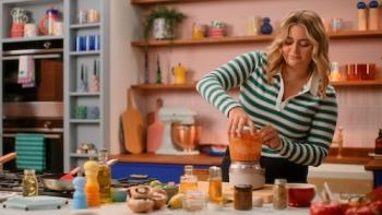 Dish It Out TV show screenshot 1: Ramsay wears a green-and-white striped shirt while standing in a pink kitchen, sealing the lid on a food processor.