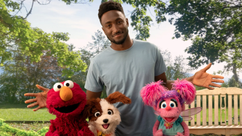 Marques Brownlee poses in a sunny park with Elmo, Tango, and Abby Cadabby