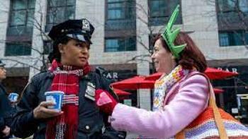 Elsbeth: A woman wearing a statue of liberty foam crown talks animatedly to a female police officer. 