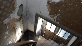 Escape to the Chateau TV show screenshot 3: Spiral wood staircase with peeling wall paper on walls around window.