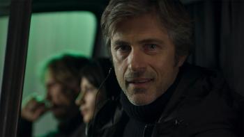 Kim Rossi Stuart looks into the camera smirking as he sits in a van. He wears an earpiece.