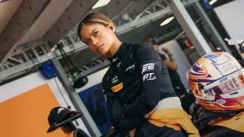 F1: The Academy TV show screenshot 2: Bianca Bustamente stands by car in black and orange livrey.