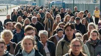 A huge group of adults and teens stands close together waiting and looking nervous