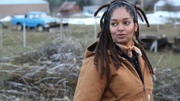 Farm Dreams TV Show: Indy Officinalis, a female Black farmer, stands on a farm field