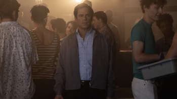Fellow Travelers TV show screenshot 4: An older Hawks stares forward surrounded by LGBT+ men in bar. 