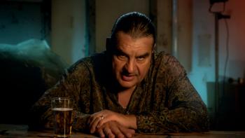 Ferry TV show screenshot: A man leans over a bar counter next to a bar looking seriously at the camera.