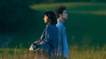 First Love TV show: A Japanese couple are seen standing in a grassy field, they are standing shoulder to shoulder but facing different directions with