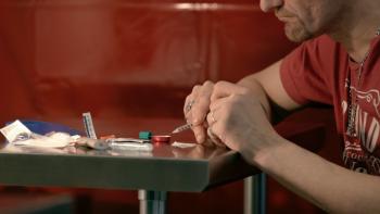 Follow This Series: A man sticks a syringe into a substance mixed up in a metal dish; on the table in front of him are a lighter and a bag of white powder. 