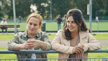 Football Parents TV show screenshot: Two middle-aged women hold coffee cups outside, leaning on a fence with expressions of dismay on their faces