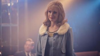 Star Gemma Arterton as Barbara Parker wears a pale blue, fur-trimmed coat. She stands in a hazy spotlight