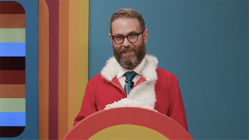 Game Changer TV show screenshot 1: Host Sam Reich smiles while standing at a colorful podium while wearing a Santa Suit without the hat