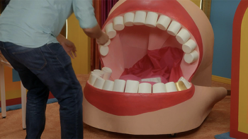Game Changer TV show screenshot 3: A contestant is seen from behind as they crouch down, throwing something into a giant mouth prop
