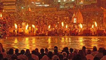 The Ganges with Sue Perkins: The Ganges riverbank with crowds of people lit up by an orange glow from small fires.