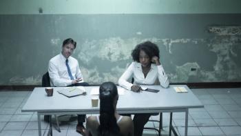 Joe Dempsie and Tamara Lawrence interrogate Shernet Swearine at a table. Files are strewn across the table.