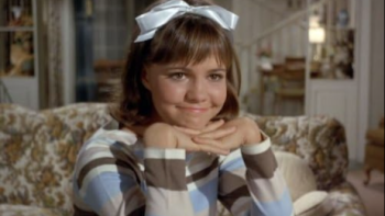 Gidget screenshot 1: Gidget with a white bow, smiling, seated in a cozy living room.