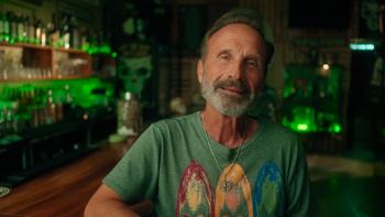 Glitter and Greed: The Lisa Frank Story TV show screenshot 1: James Green wears a green t-shirt and sits at a bar, facing the camera.