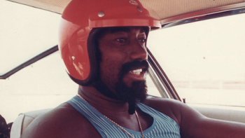 Goliath 2023 screenshot 3: Wilt Chamberlain wears an orange helmet as he drives a race car. 