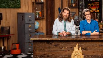 Good Mythical Morning TV show screenshot: Two men sit at a desk in an "office" with a microphone in front, set against a cozy background.