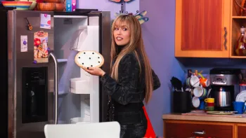 Hannah Montana 20th Anniversary Special screenshot 2: Miley Cyrus in Hannah Montana's kitchen holds a pie in her hand with the fridge door open.