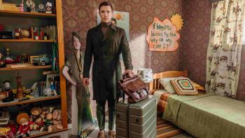 Happiness TV show screenshot 1: Harry Naughton stands in a childhood bedroom. He wears a dark green coat, turtleneck, gray pants, and brown shoes.