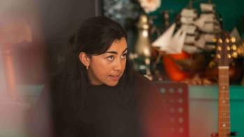 Happiness TV show screenshot 2:Marshayla Christie sits on a chair. She wears a dark turtleneck. The neck of a guitar and a model of a ship sit by her.