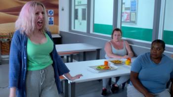 Hard Cell TV show screenshot 3: A pink-haired woman in a green shirt stands in a cafeteria, shouting, as two seated women look on.