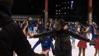 Harlem Ice TV show screenshot 2: Coach stands in an ice rink filled with young black girls, directing the kids through practice.