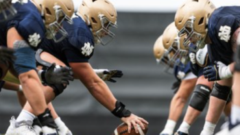 Here Come the Irish screenshot 2: Athletes on field in blue and gold uniforms bent over for football pass. 