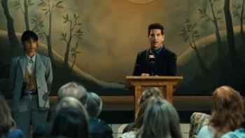 His & Hers TV show screenshot 3: Richard stands at a podium in front of a small audience while Priya is off to one side