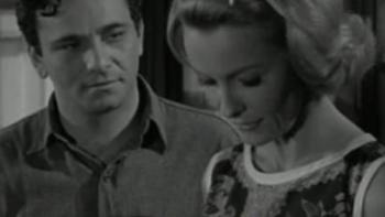 A man with dark hair looks at a blonde woman expectantly, she is glancing down.